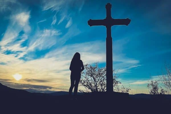 Woman standing in front of a cross at sunset