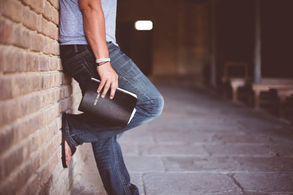 Man leaning against wall holding bible