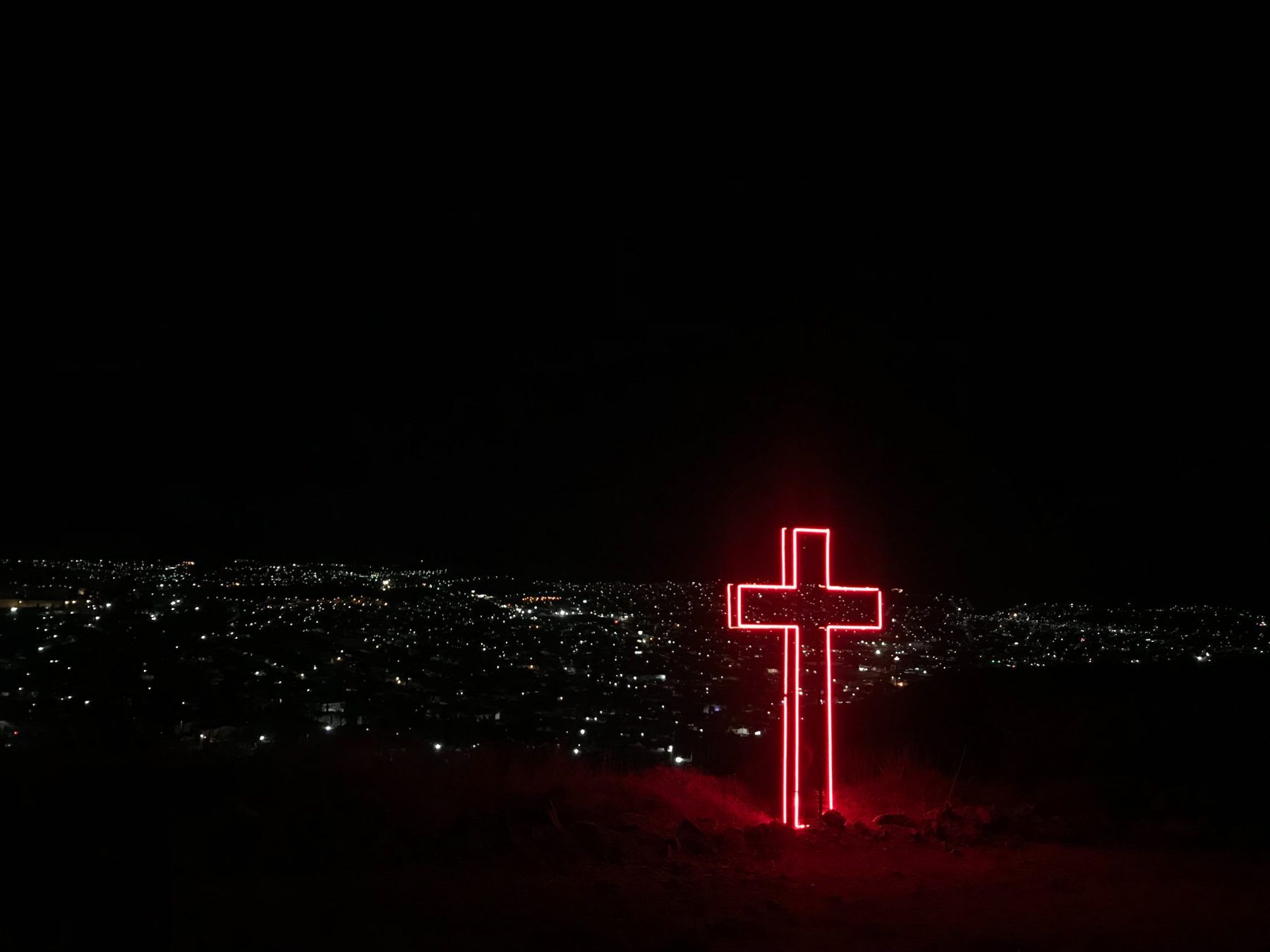 Neon cross overlooking city at night
