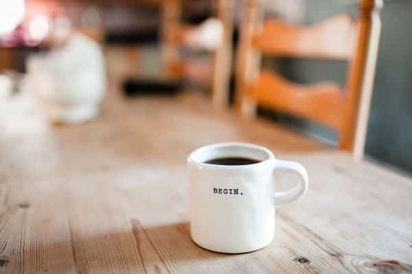 A white coffee mug with “begin” written on it on a wooden table.