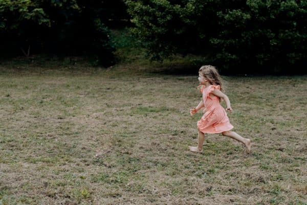 Little girl running through a grassy field in a sleeveless dress