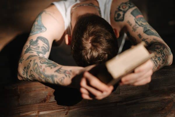 Tattooed man praying while holding a book
