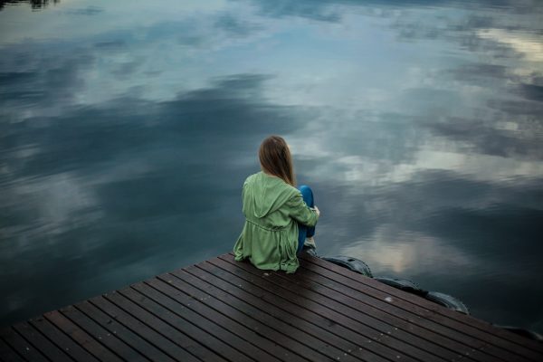 Woman sitting in silence on lake dock
